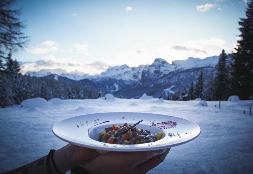 Piatto di selvaggina impiattato all’aperto con sfondo innevato
