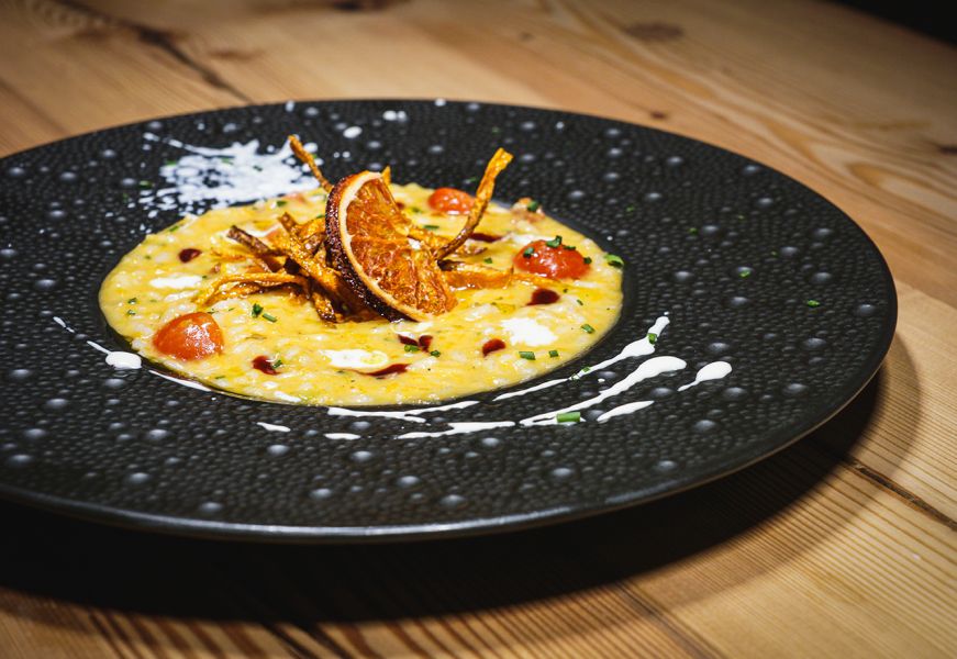 Risotto con agrumi e chips croccanti servito su piatto scuro